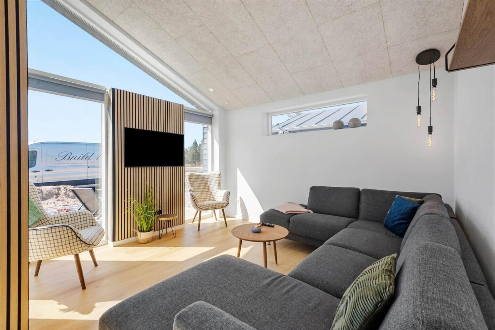 Wohnzimmer mit grauem Sofa, Holzboden und großem Fenster zur Außenseite.