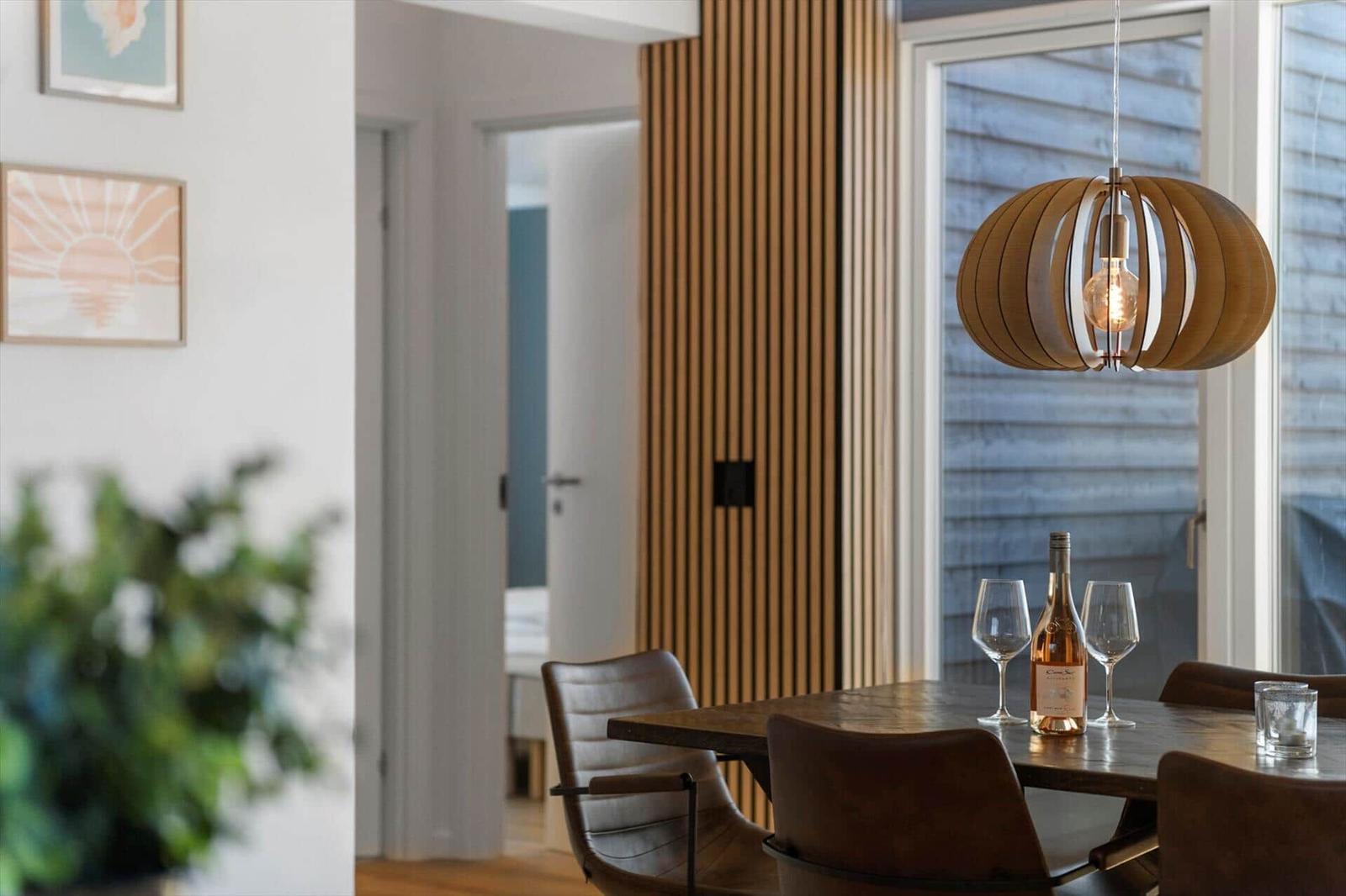 Esstisch mit Weinflasche und Gläsern unter einer Holzlampe.