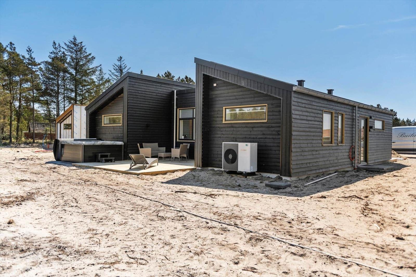 Moderne Holzhütte mit Terrasse, Gartenmöbeln und Außendusche. Umgeben von Wald und Sand.