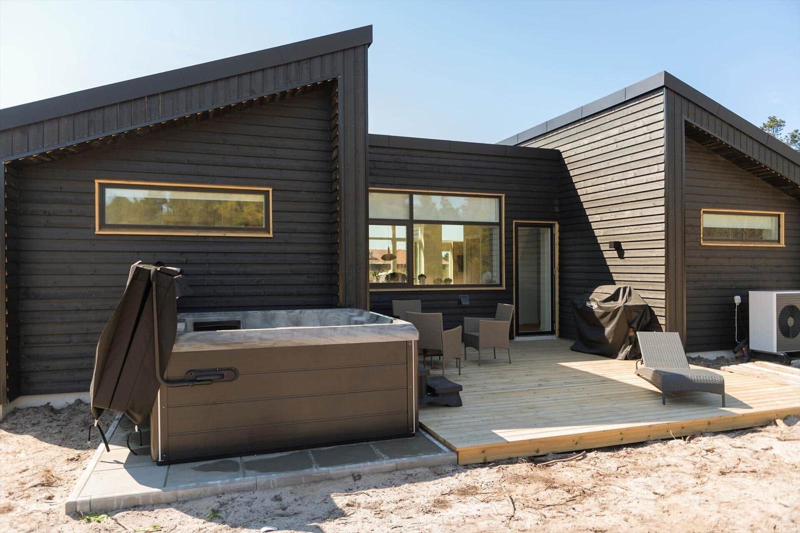 Moderne Holzhütte mit Whirlpool, Terrasse und Gartenmöbeln.