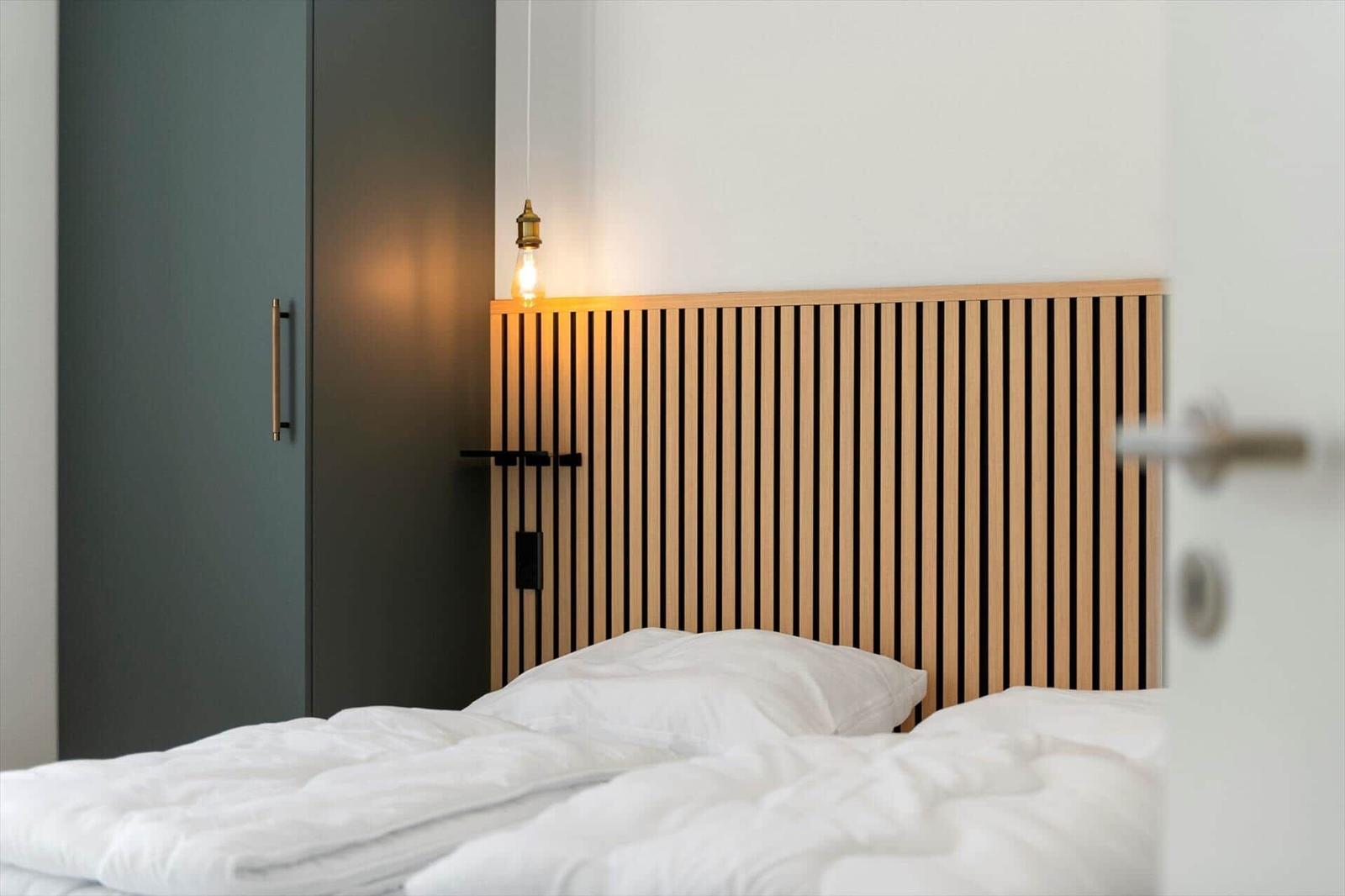 Schlafzimmer mit Holz-Kopfteil, weißer Bettwäsche und schwarzem Schrank.