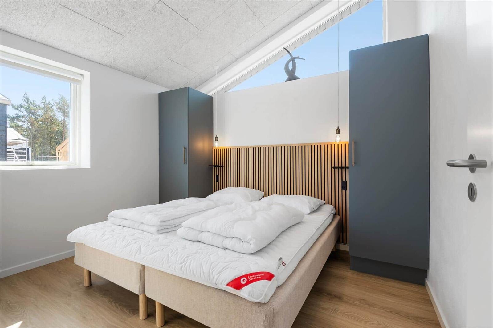 Schlafzimmer mit Doppelbett, Holzfußboden und großen Fenstern.