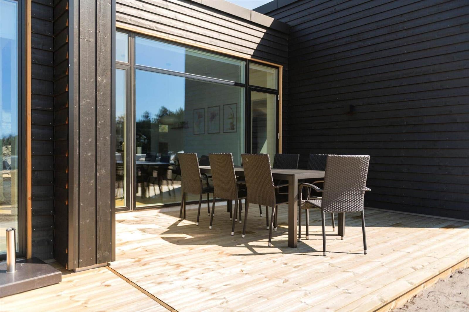 Terrasse mit Tisch und Stühlen vor modernem Haus mit Glasfront.