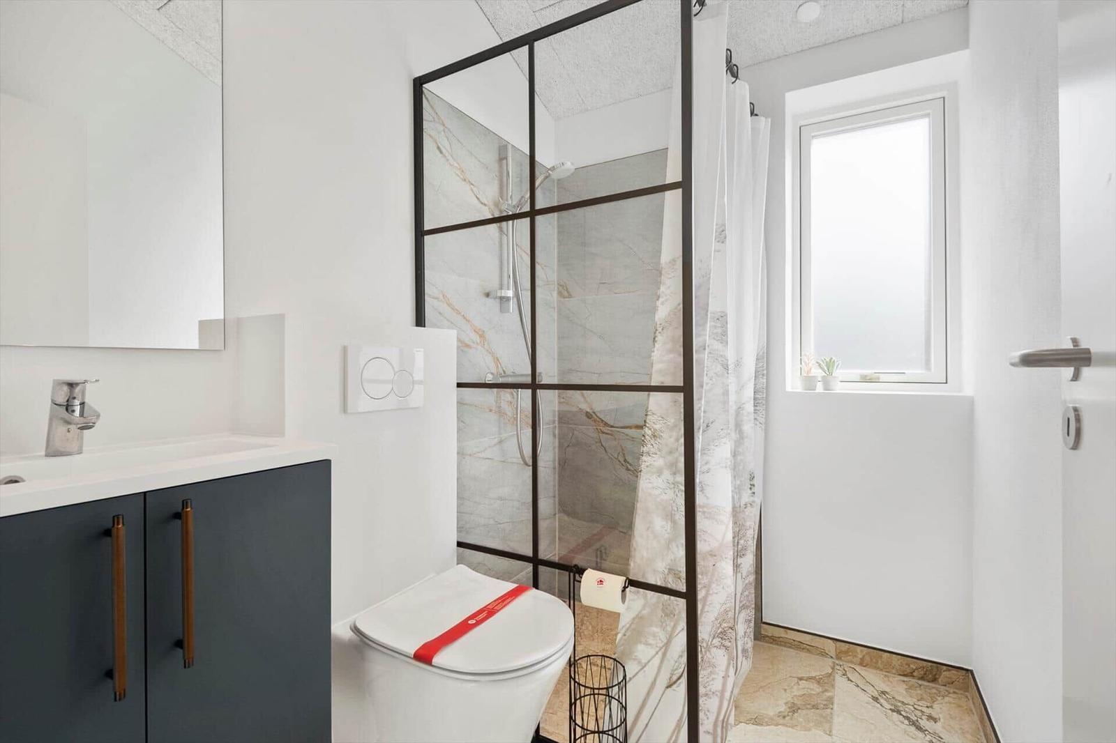 Badezimmer mit Dusche, Toilette und Waschbecken. Fenster und Marmorfliesen.