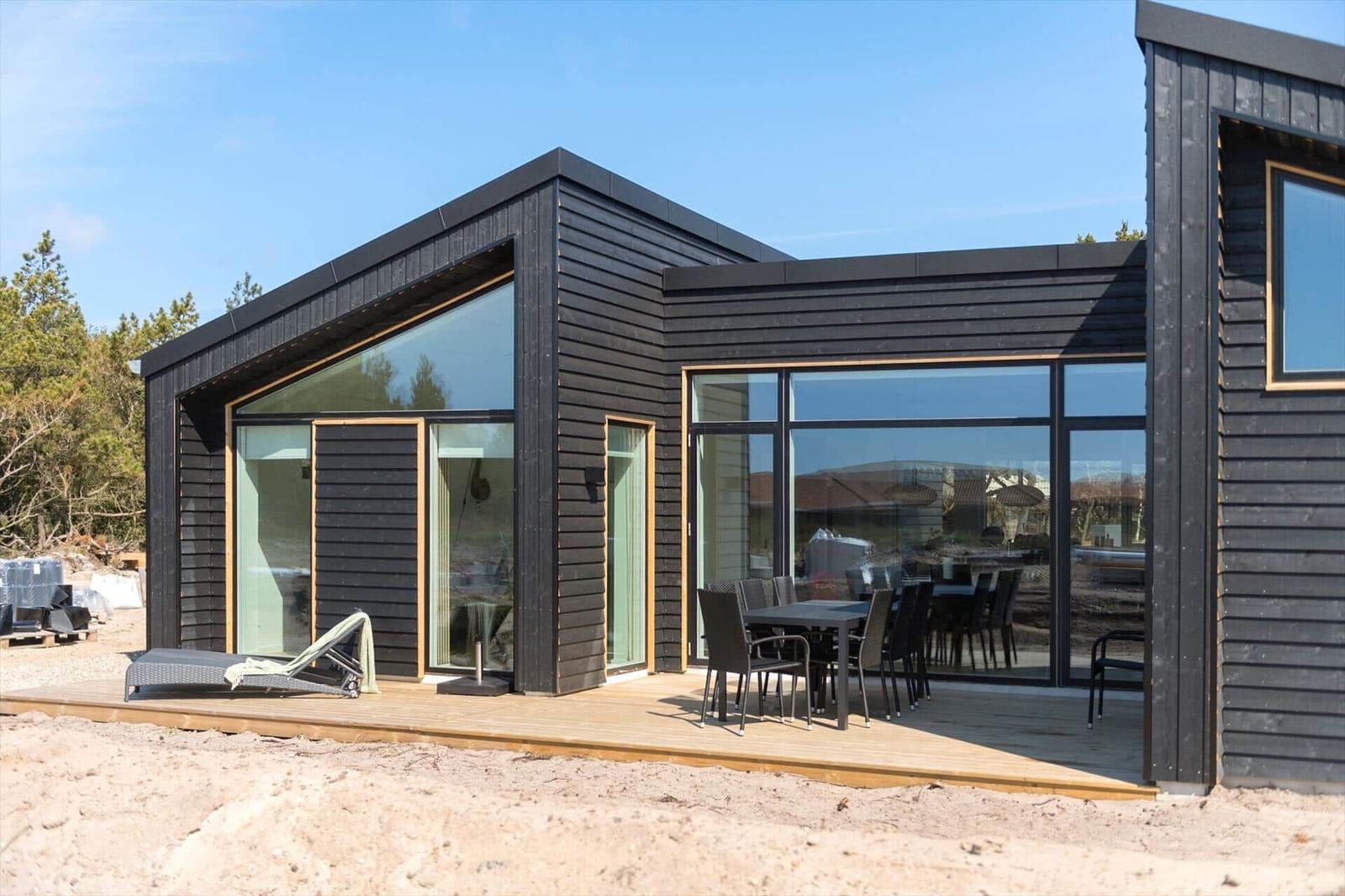 Moderne Holzhütte mit großem Terrassenbereich und Sitzgelegenheiten.