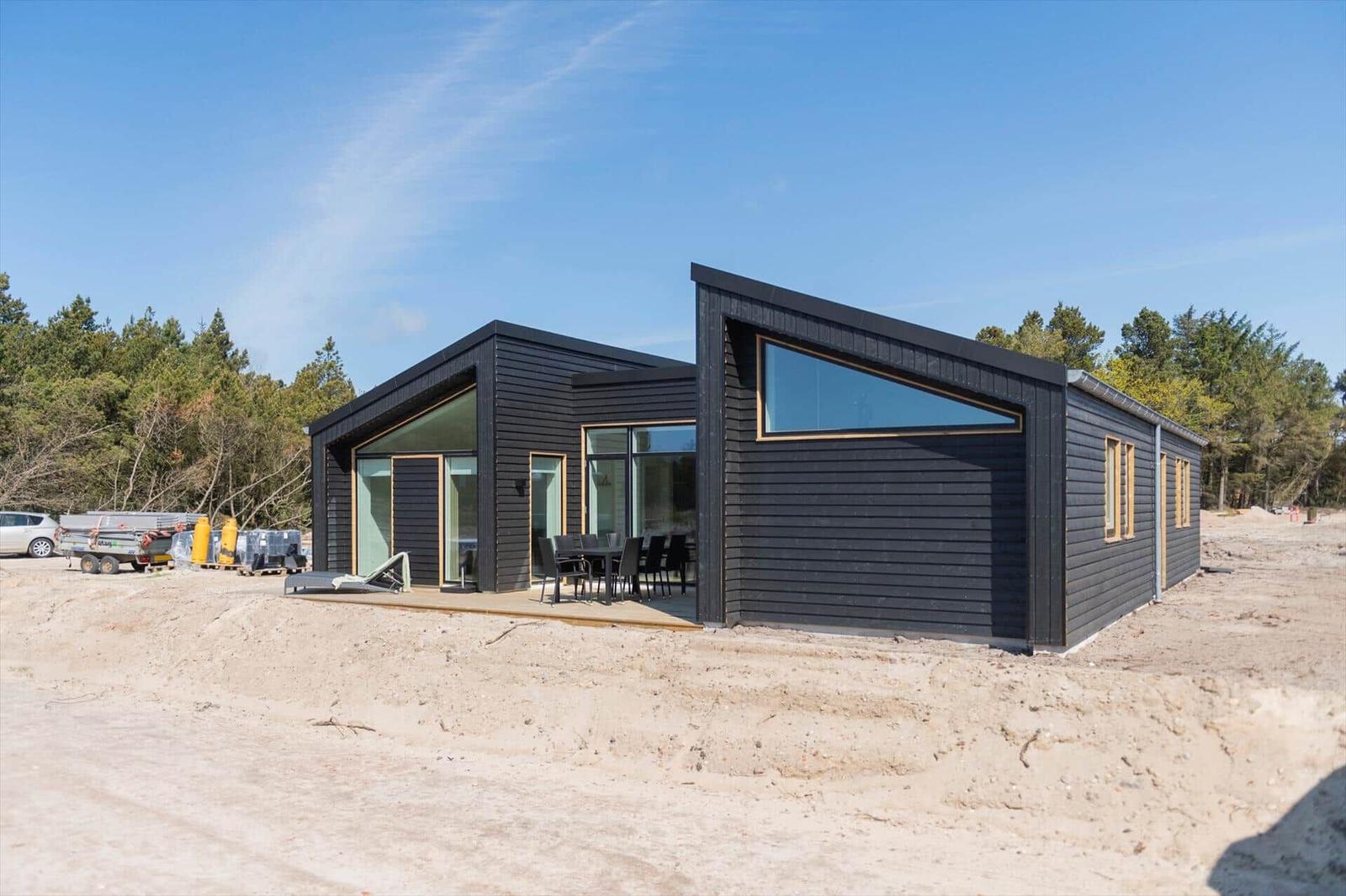 Moderne schwarze Hütte mit großem Glasbereich und Außenterrasse im Wald.