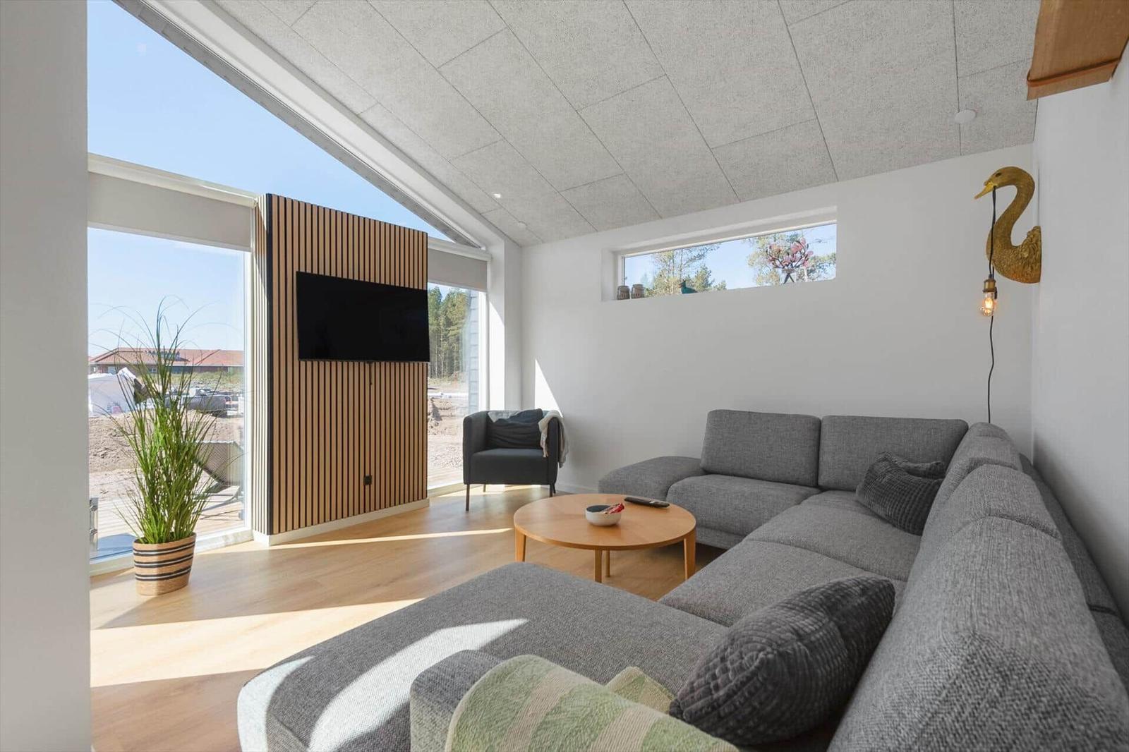 Ein Wohnzimmer mit grauem Sofa, runder Tisch und großen Fenstern.