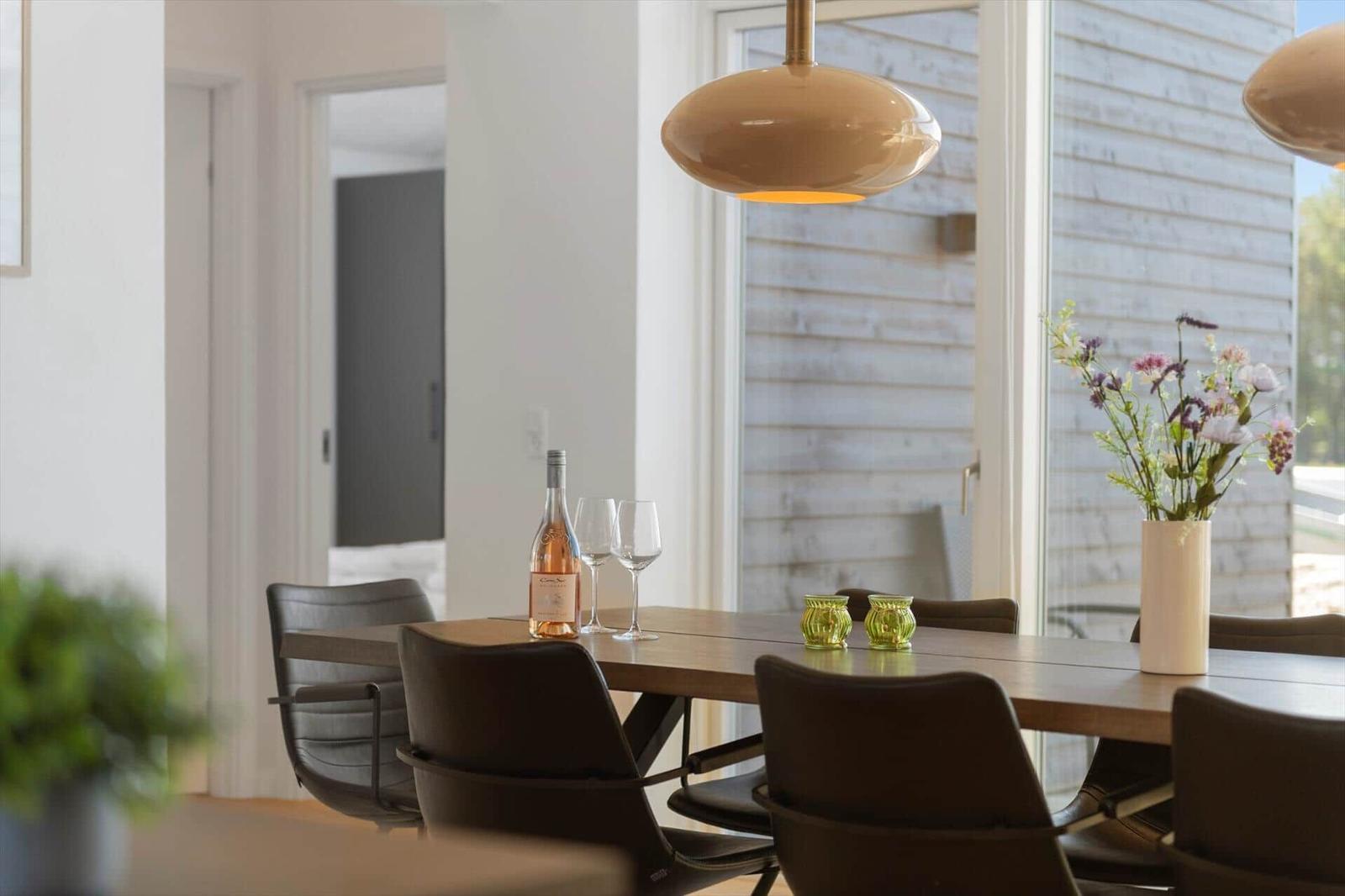 Esszimmer mit Holztisch, Stühlen und Blumenarrangement. Hängelampe und Fenster sichtbar.