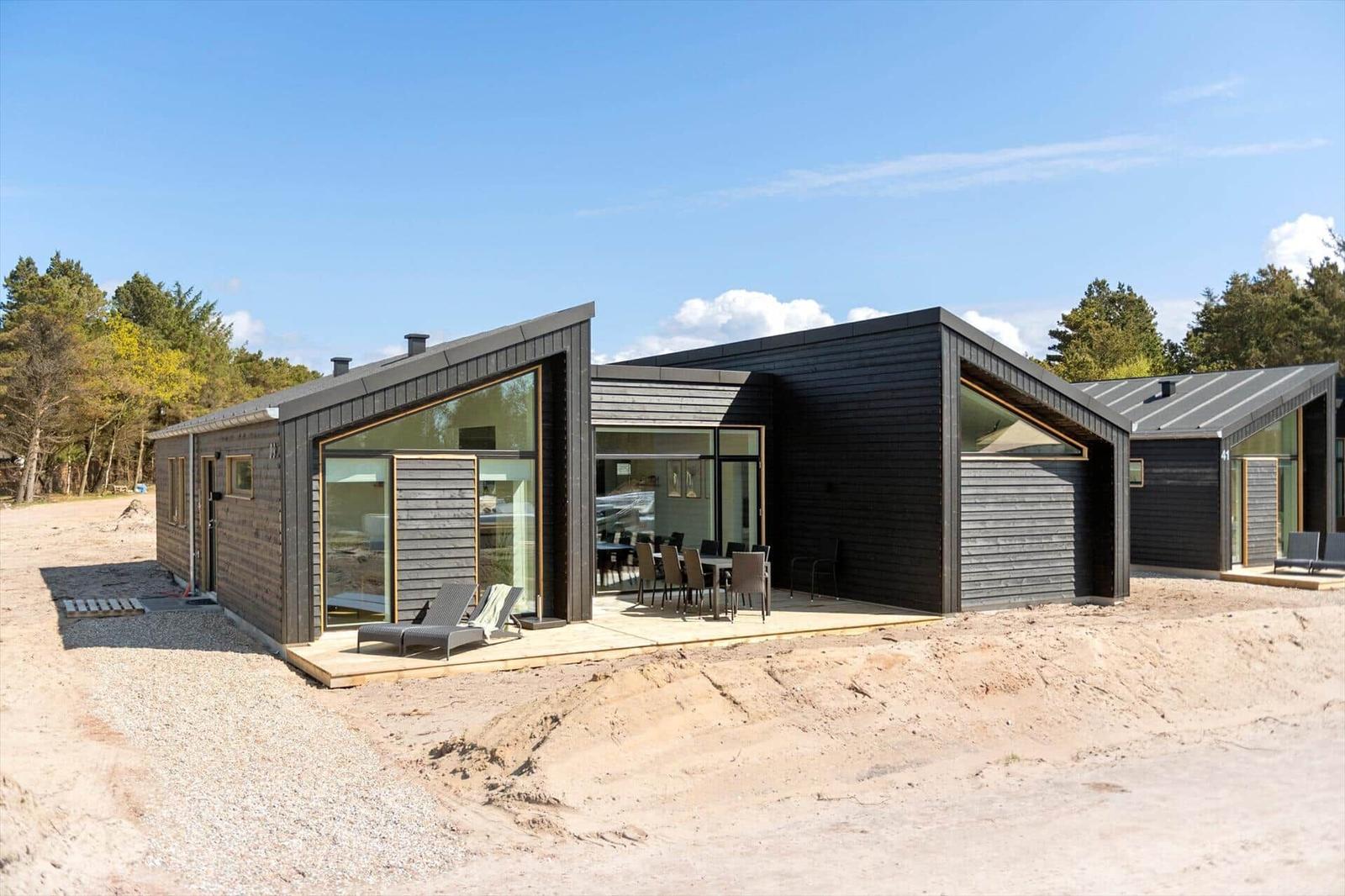 Moderne Holzhütte mit großem Terrassenbereich und Sitzgelegenheiten im Freien.