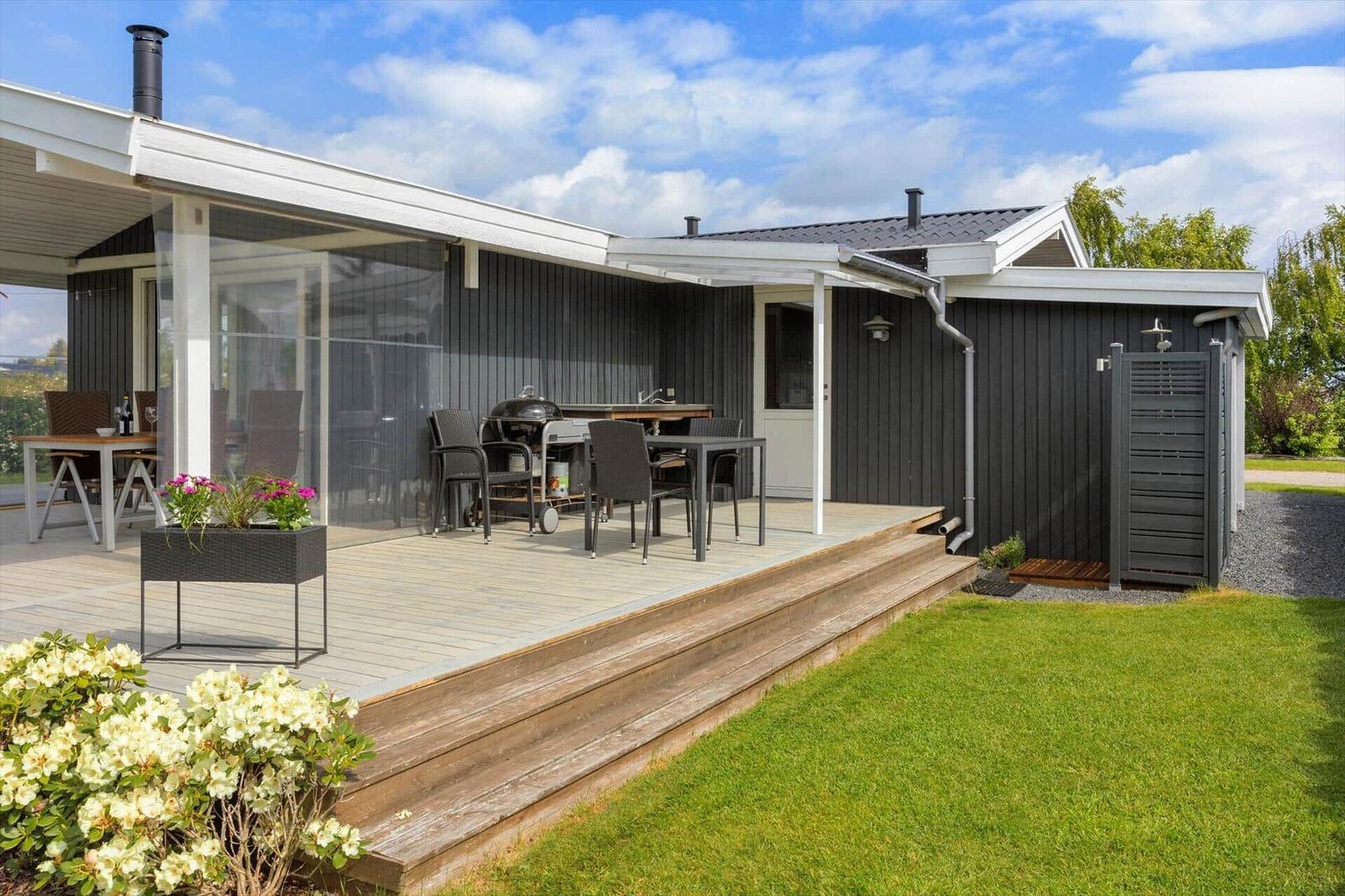 Deck with grill, table and chairs. Black wood wall and green lawn.