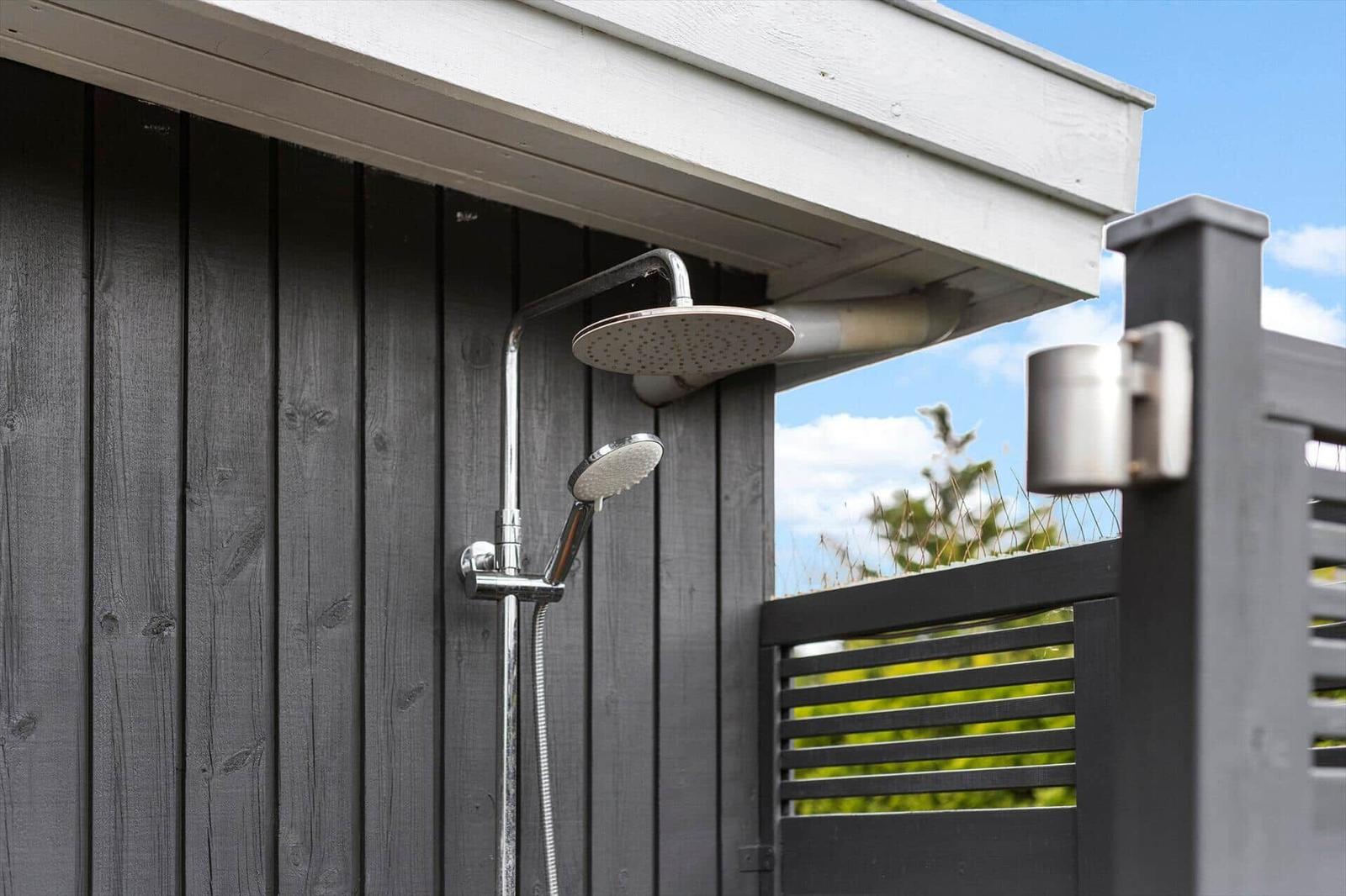 Outdoor shower with shower head and handheld shower at gray wooden house.