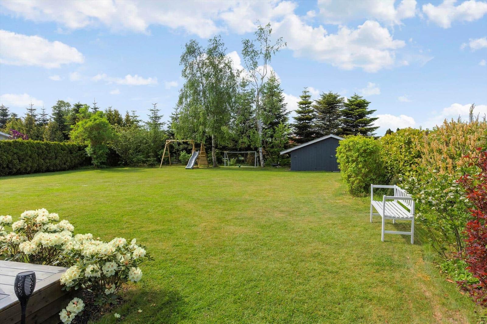 Large garden with lawn, play equipment, benches, and plants.