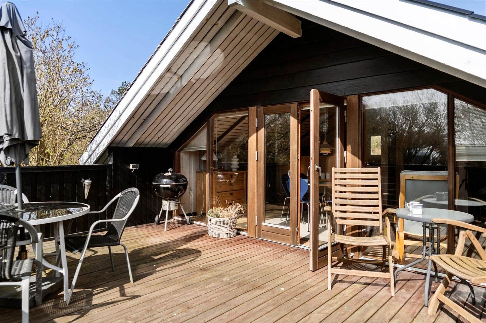 Terrasse mit Sitzgelegenheiten und Grill, Zugang zum Haus durch Schiebetüren.