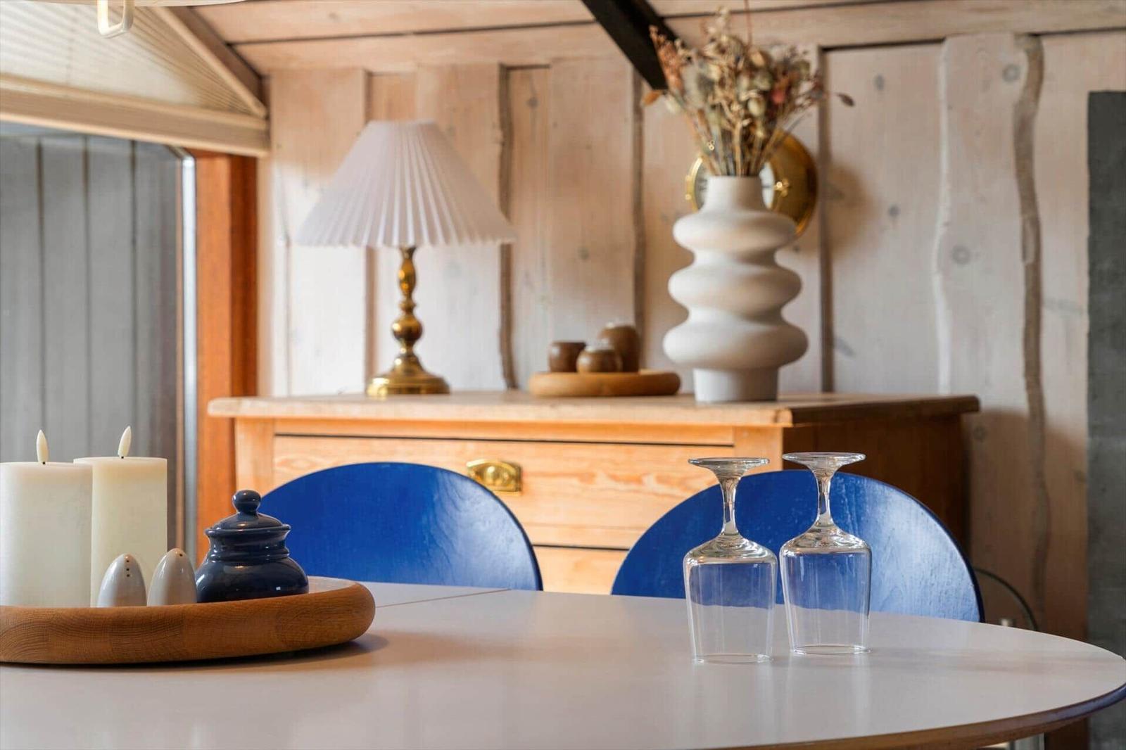 Runder Tisch mit blauen Stühlen, Kerzen und Gläsern vor Holzwand und Schrank.