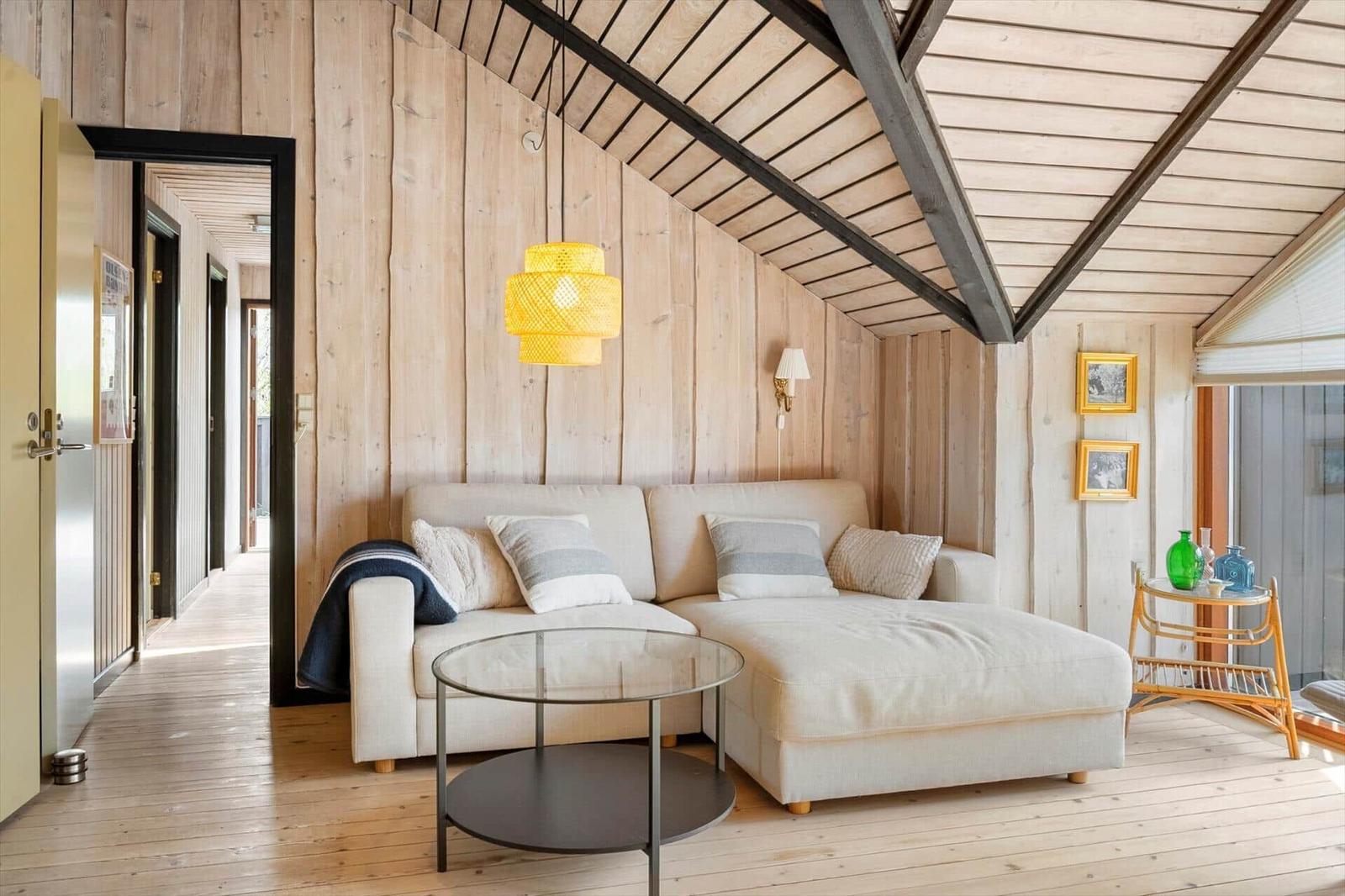 Wohnzimmer mit Sofa, Tisch und Holzwand. Decke mit Balken und Lampe.