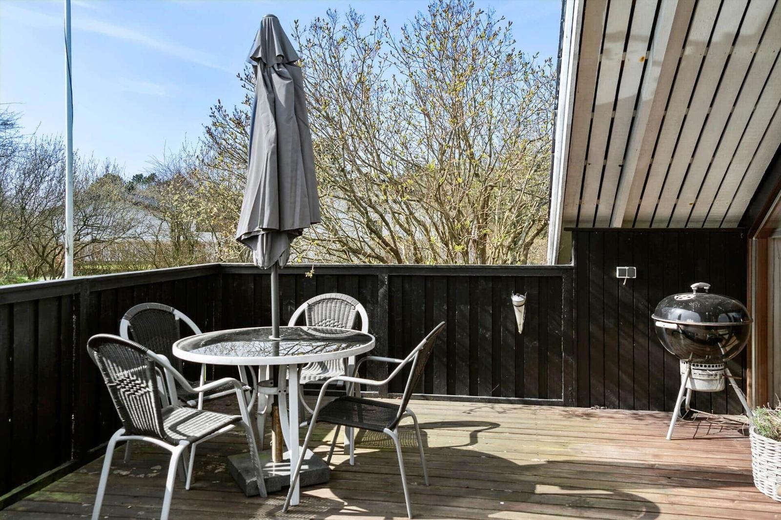 Terrasse mit Tisch, Stühlen, geschlossenem Sonnenschirm und Grill.