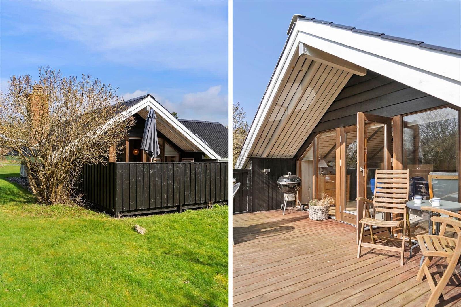 Holzhaus mit Terrasse, Grill und Sitzgelegenheiten. Grünfläche und Baum im Hintergrund.