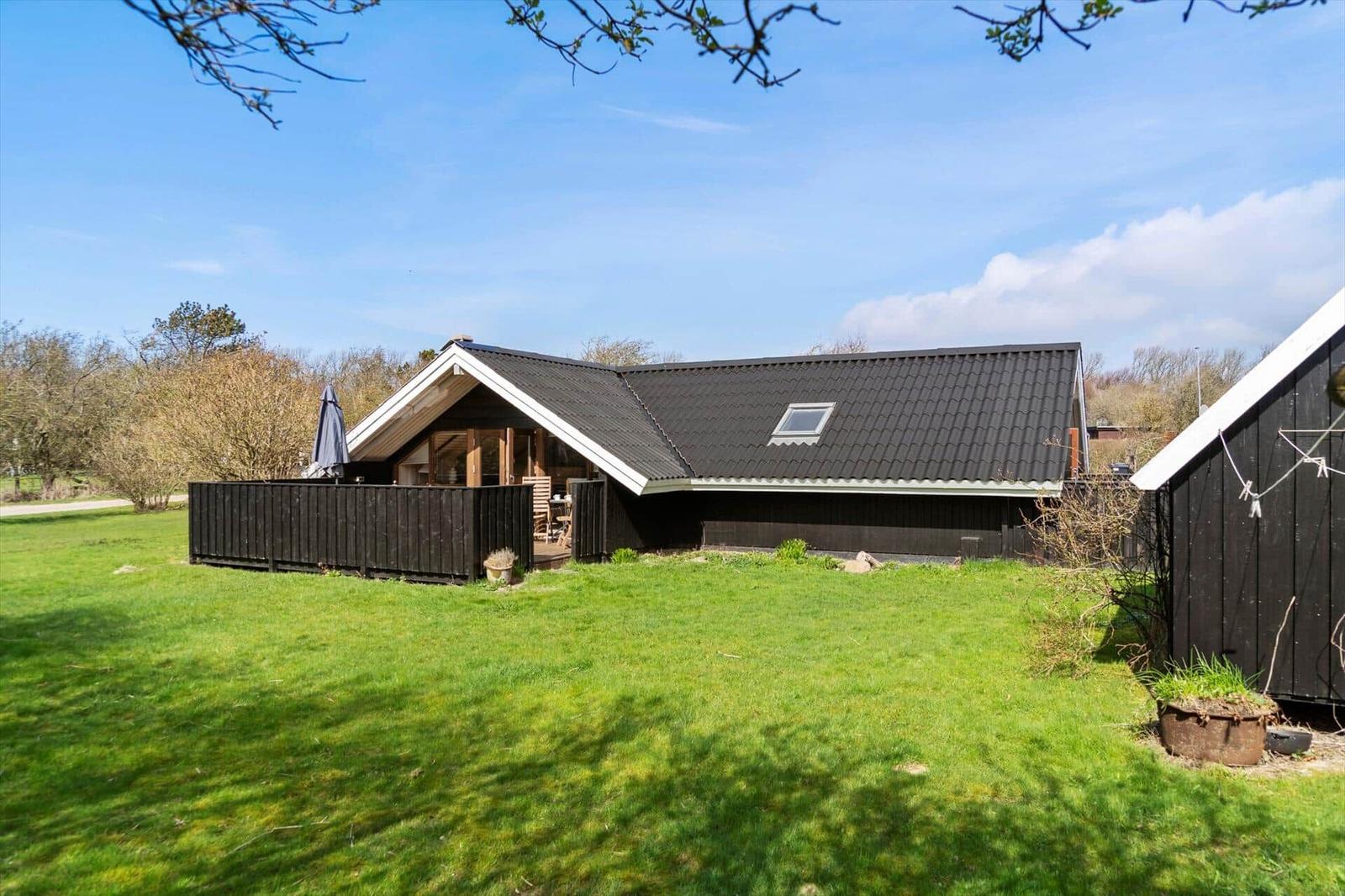 Ein Haus mit dunklem Dach und Holzverkleidung, umgeben von Gras und Bäumen.