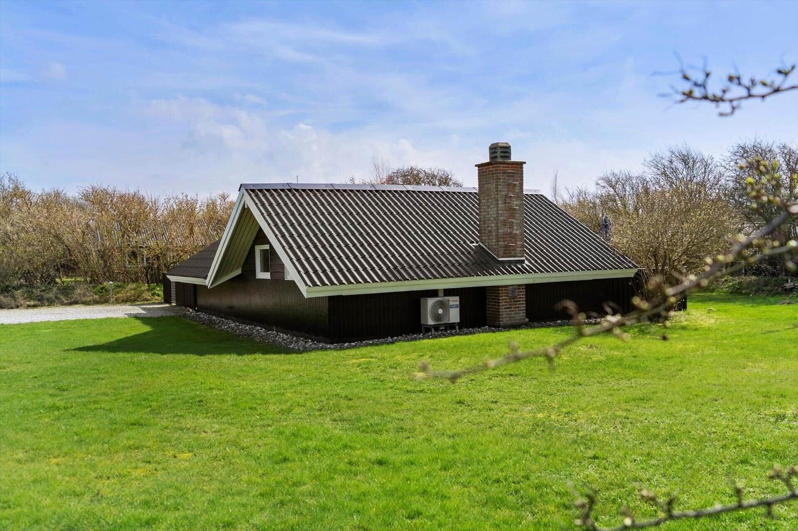 Ein Haus mit dunkler Fassade, schrägem Dach und Schornstein steht auf einer grünen Wiese.
