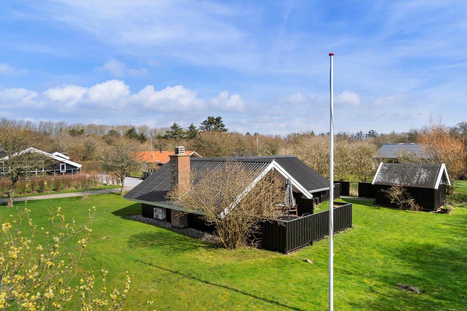 Haus mit Garten, Grillplatz und kleinem Nebengebäude unter blauem Himmel.