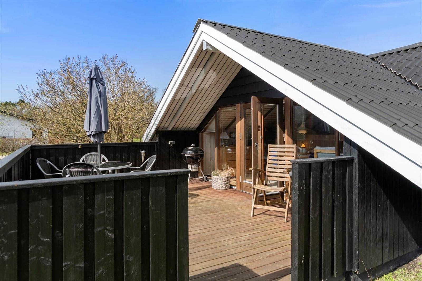 Terrasse mit Tisch, Stühlen und Sonnenschirm. Holzveranda mit Grill und Sitzgelegenheit.