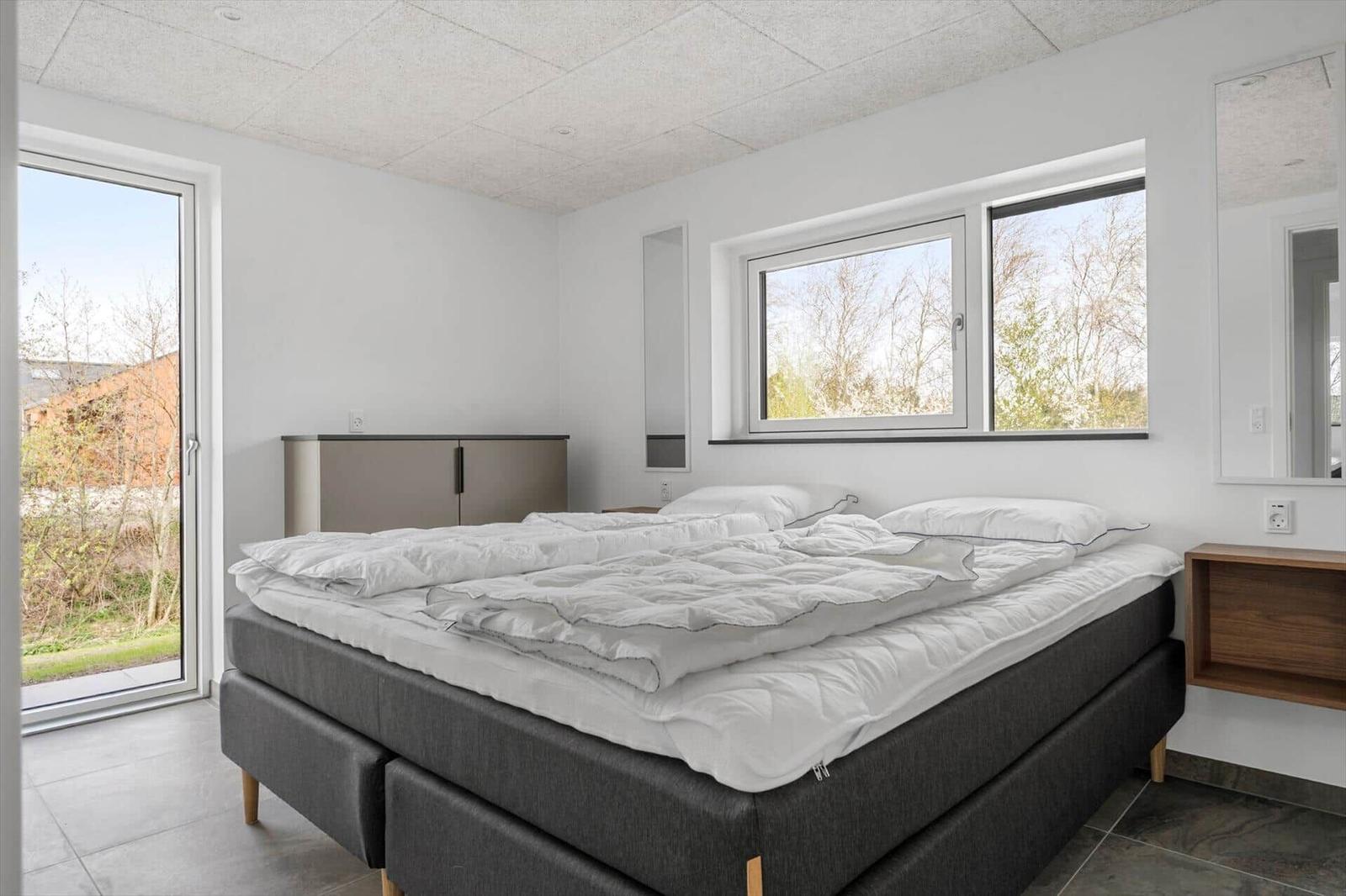 Schlafzimmer mit Doppelbett, Fenstern und Tür zur Außenterrasse.