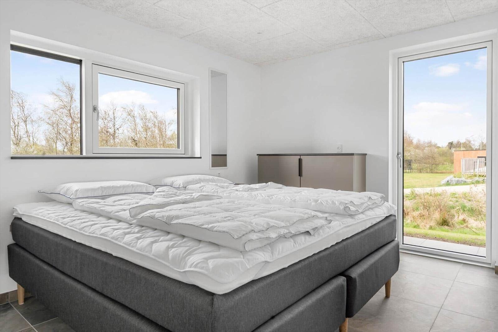 Schlafzimmer mit Bett, Fenstern und Glastür zur Außenseite.