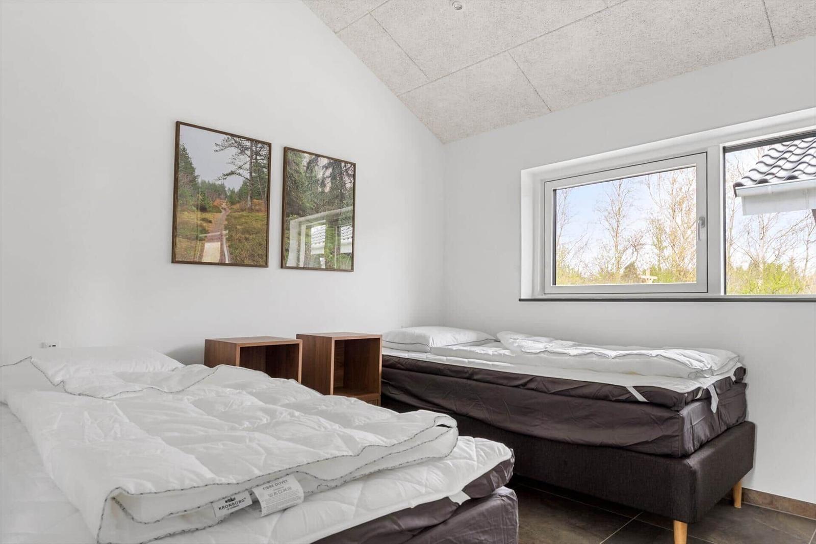 Zwei Betten mit Matratzen und Decken. Fenster mit Blick auf Bäume. Wandbilder und Nachttische.