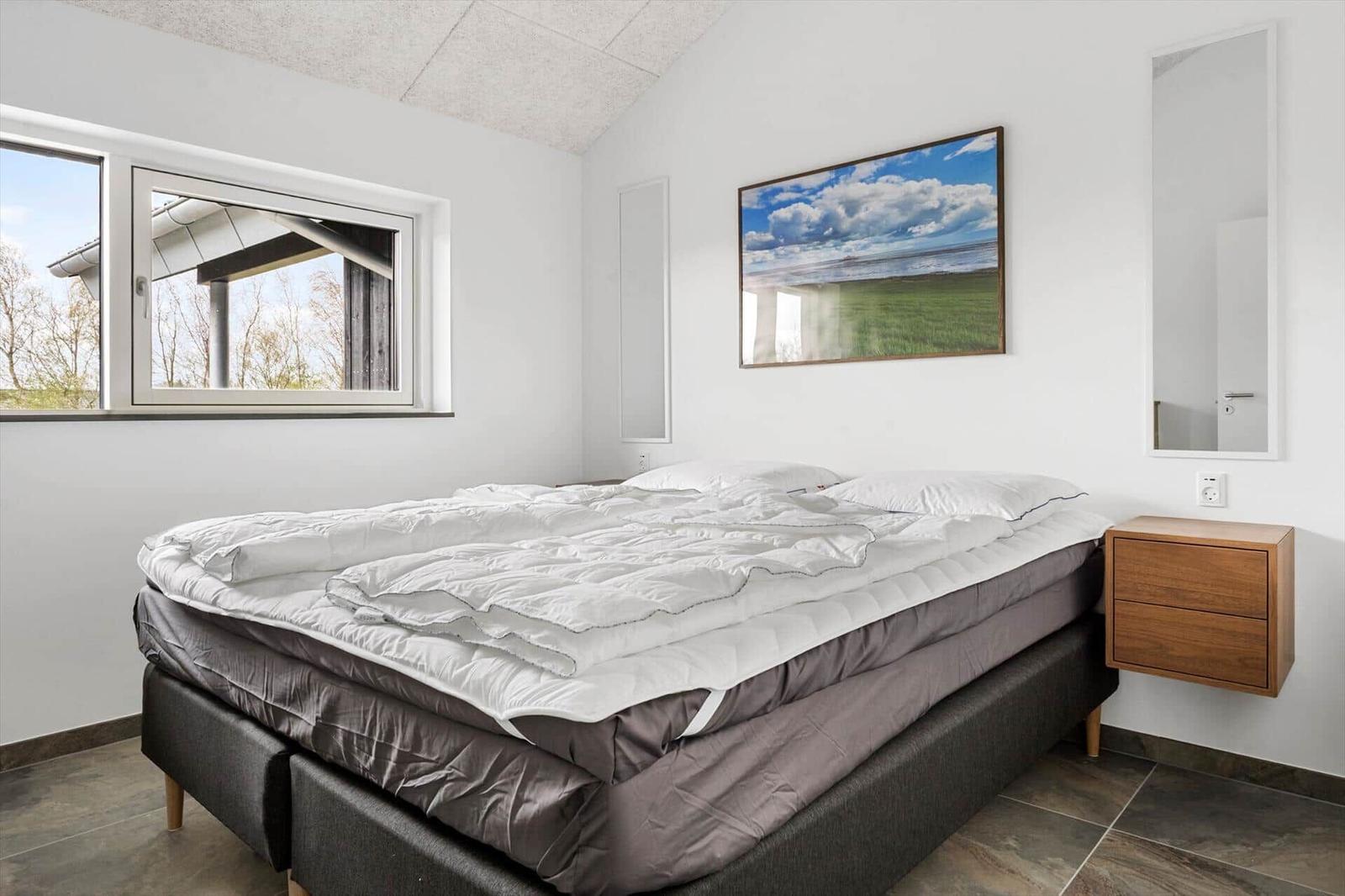Schlafzimmer mit Bett, Fenster, Wandbild und Nachttisch.
