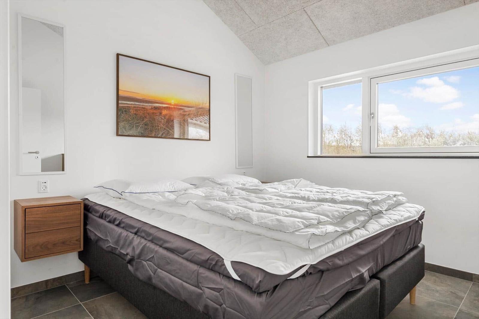 Schlafzimmer mit großem Bett, Fenster und Wandbild.