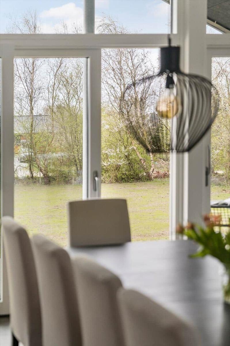 Esstisch mit Stühlen vor großem Fenster mit Blick auf Garten und Bäume.
