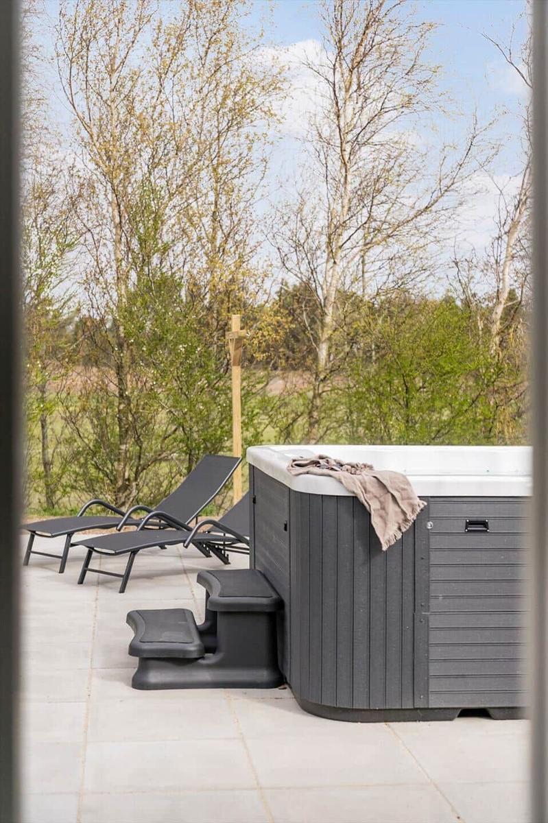 Außenbereich mit Whirlpool, Liegestühlen und Blick auf Wald.