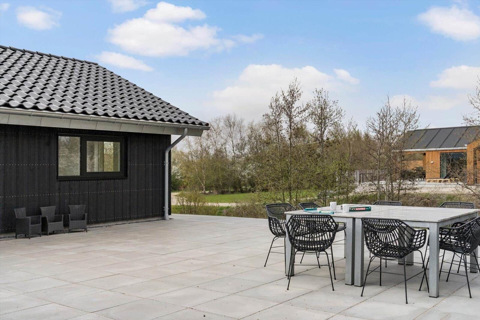 Terrasse mit Tisch und Stühlen vor einem Haus mit dunklem Holz und grauem Dach.