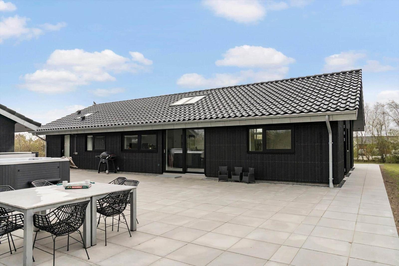 Moderne Villa mit großem Außenbereich, Grill und Hot Tub unter blauem Himmel.