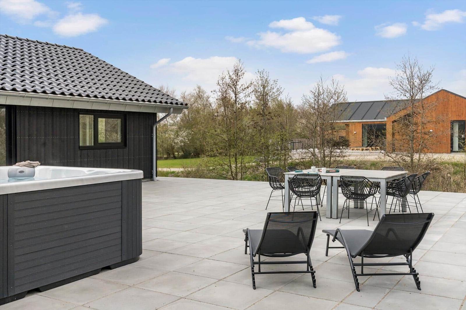 Terrasse mit Whirlpool, Esstisch und Liegestühlen. Hintergrund: Holzhaus und Wald.