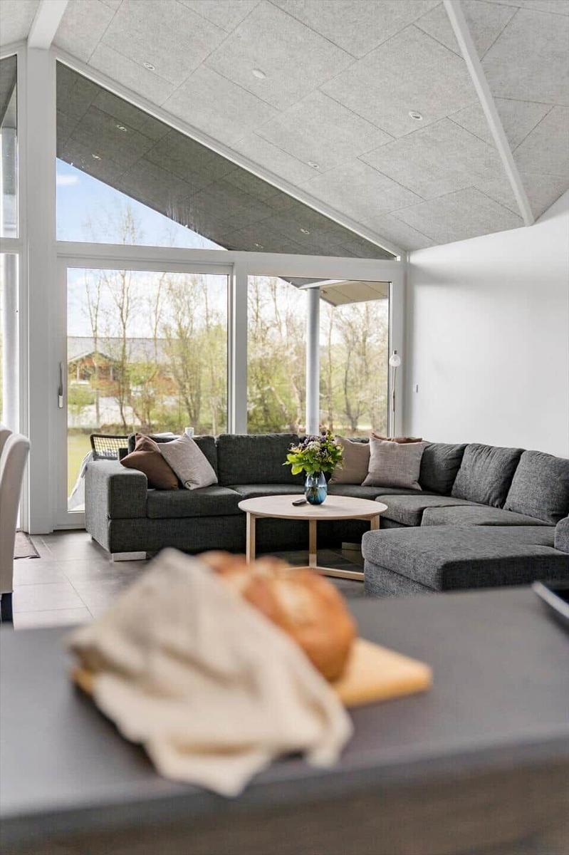 Großes Wohnzimmer mit grauem Sofa, runder Tisch und großem Fenster. Blick auf Garten.