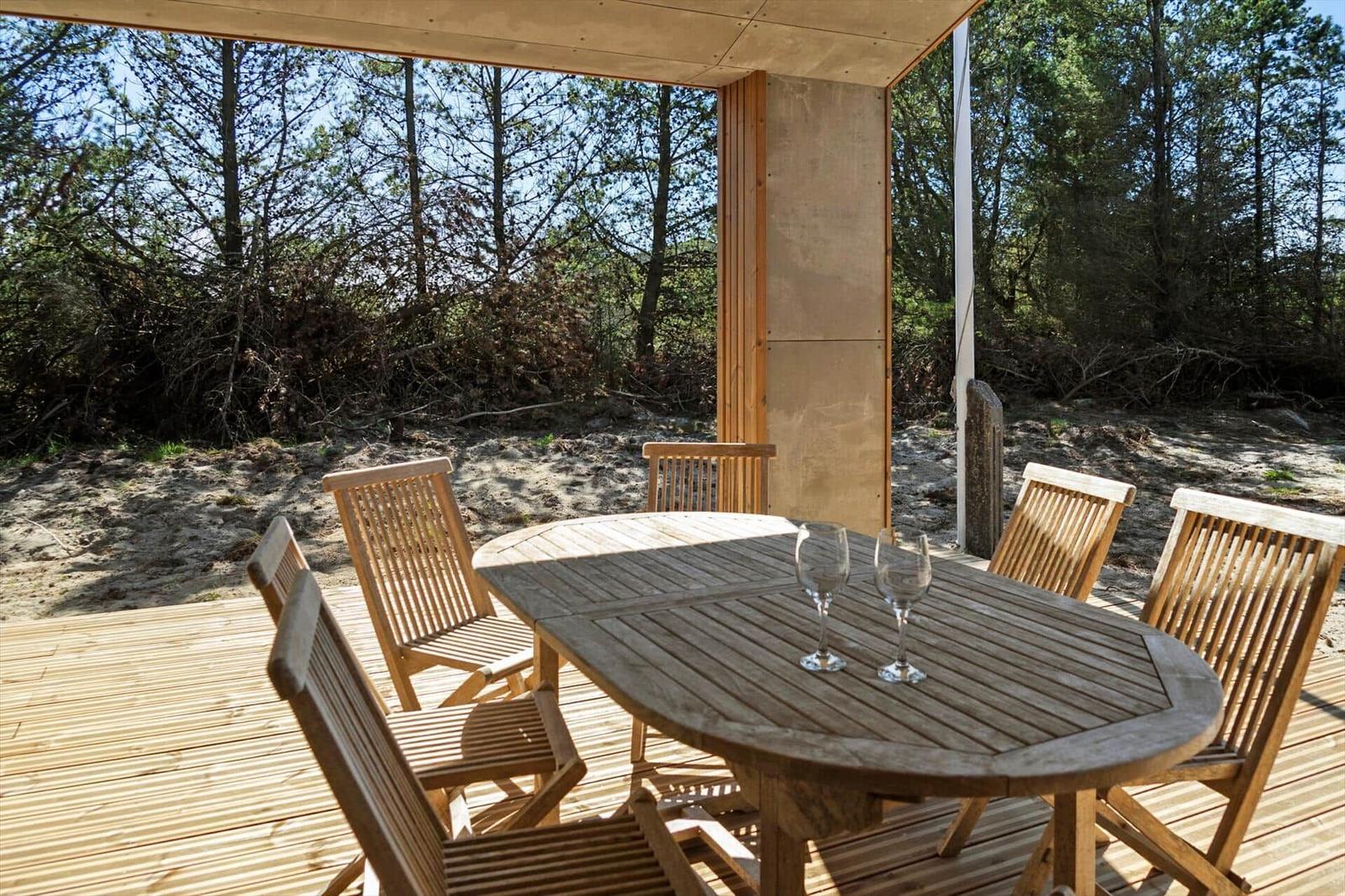 Wooden table with six chairs on a terrace with forest view.