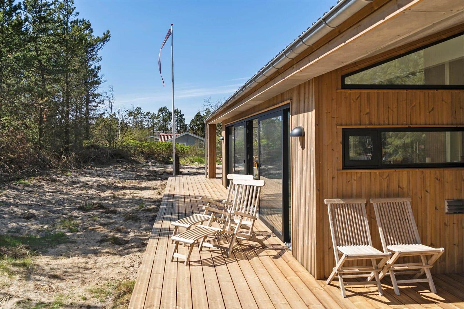 Wooden deck with chairs and flag next to a wooden house with large windows.