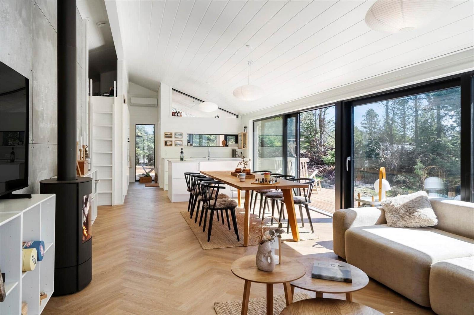 Living area with dining space, sofa, and fireplace. Large windows overlooking the garden.