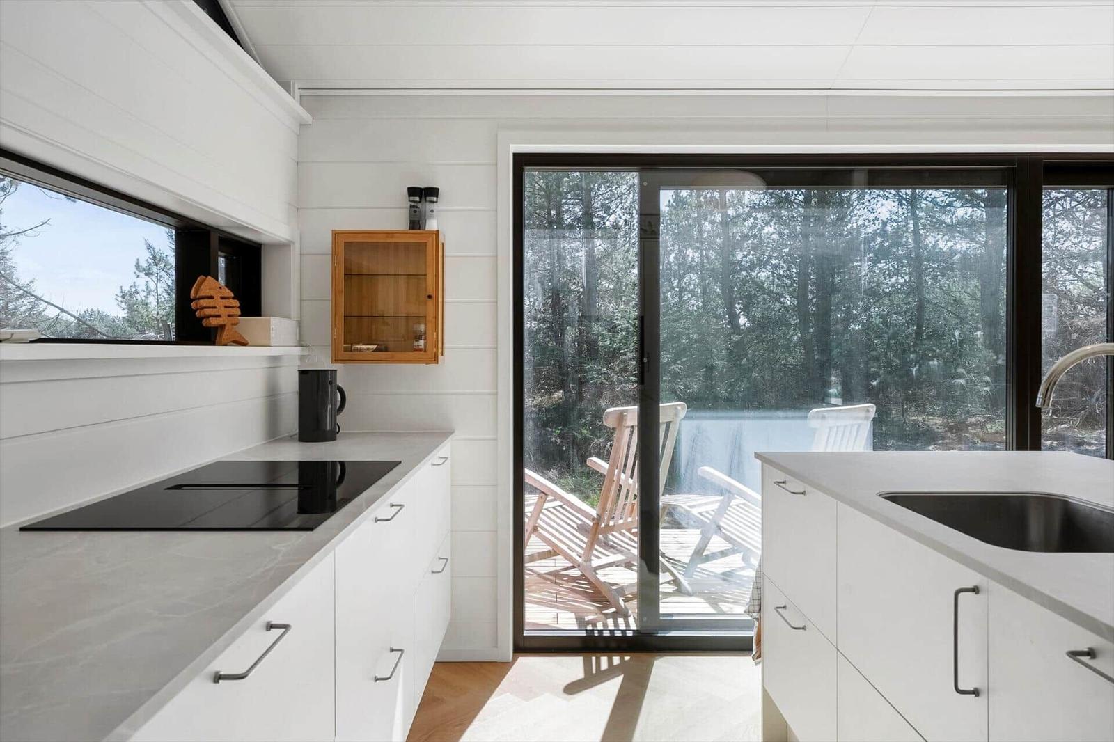 Kitchen with view of deck and forest. White cabinets, black countertop, and wooden chairs.