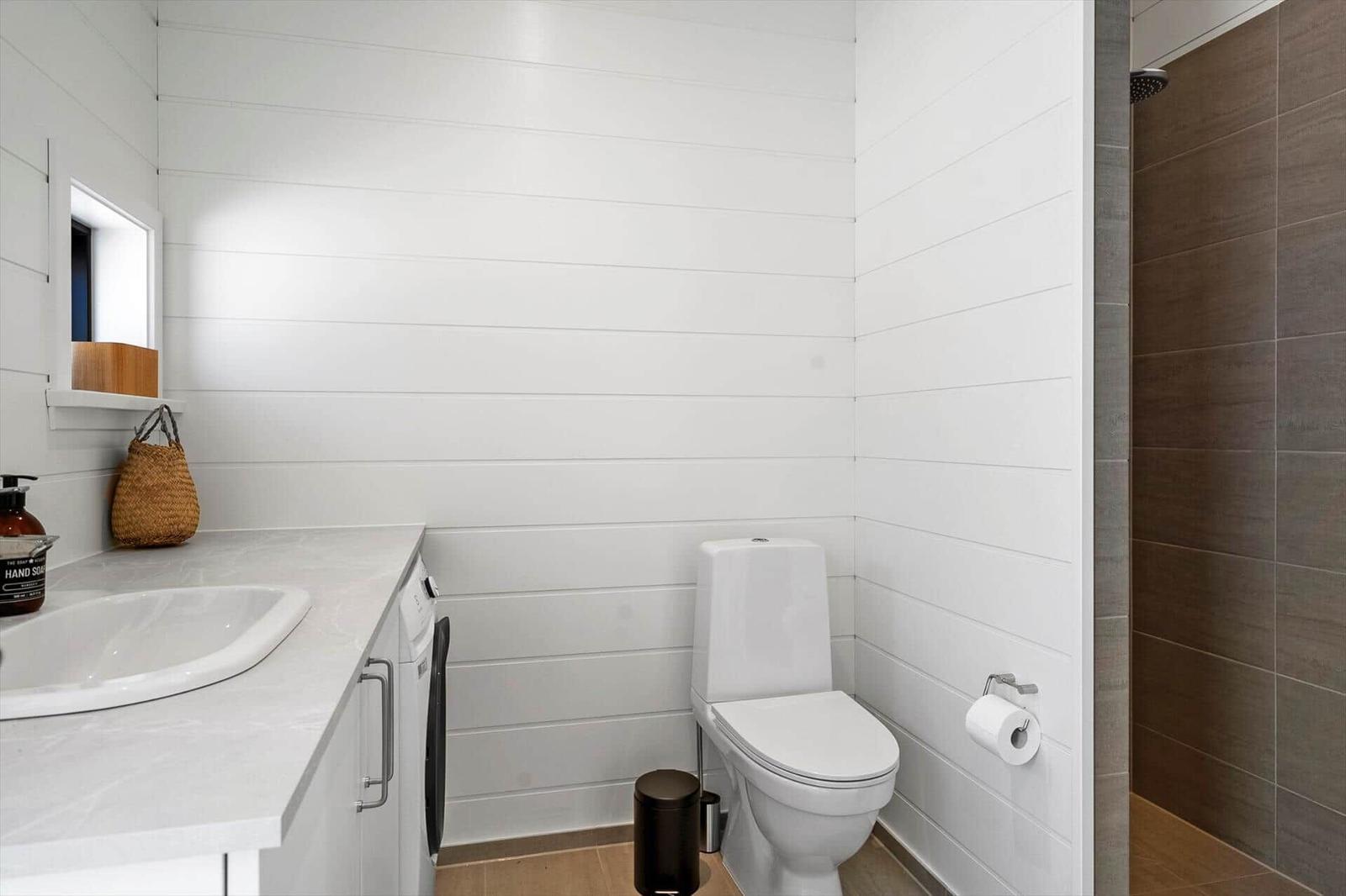 Bathroom with toilet, sink, and shower. Walls with white wood panels.