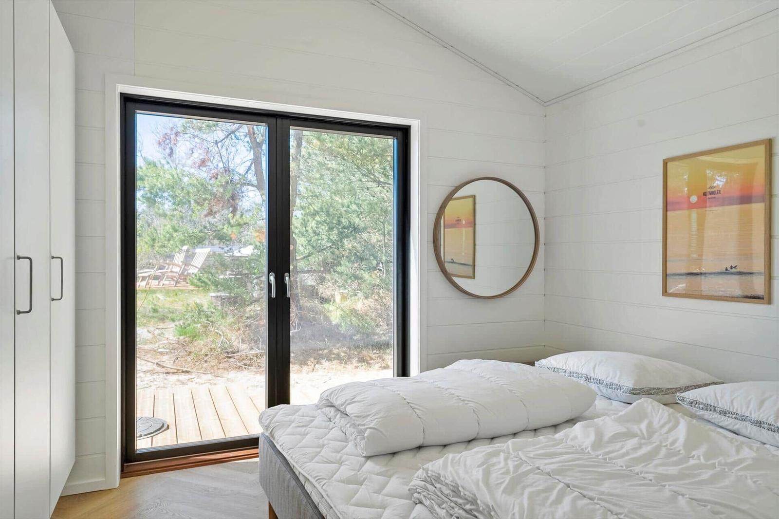 Bedroom with bed, sliding door, and wall art. Outside is a wooden deck with chairs.