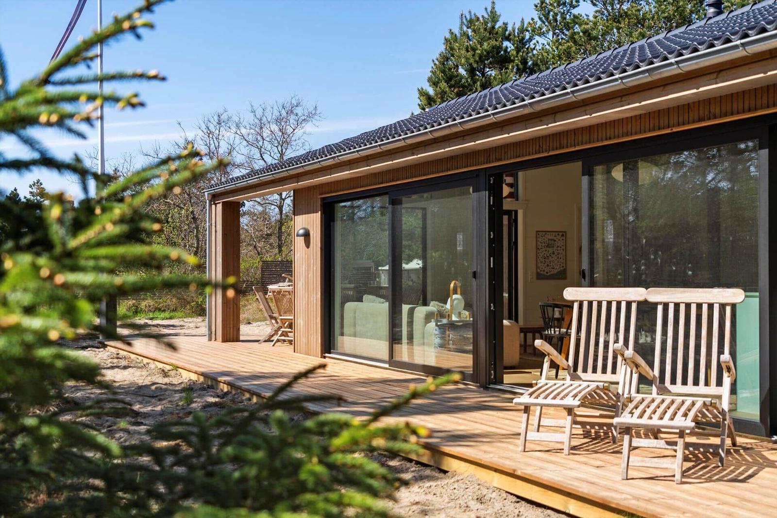 Modern villa with wooden terrace and glass facade. Two wooden chairs are outside.