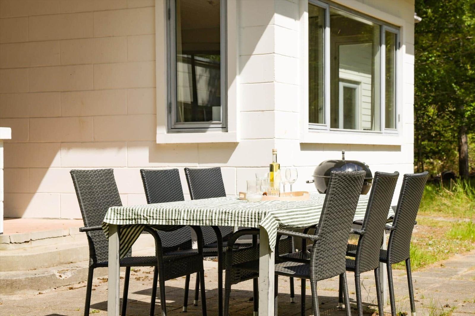 Außentisch mit sechs Stühlen und Grill vor Hauswand.