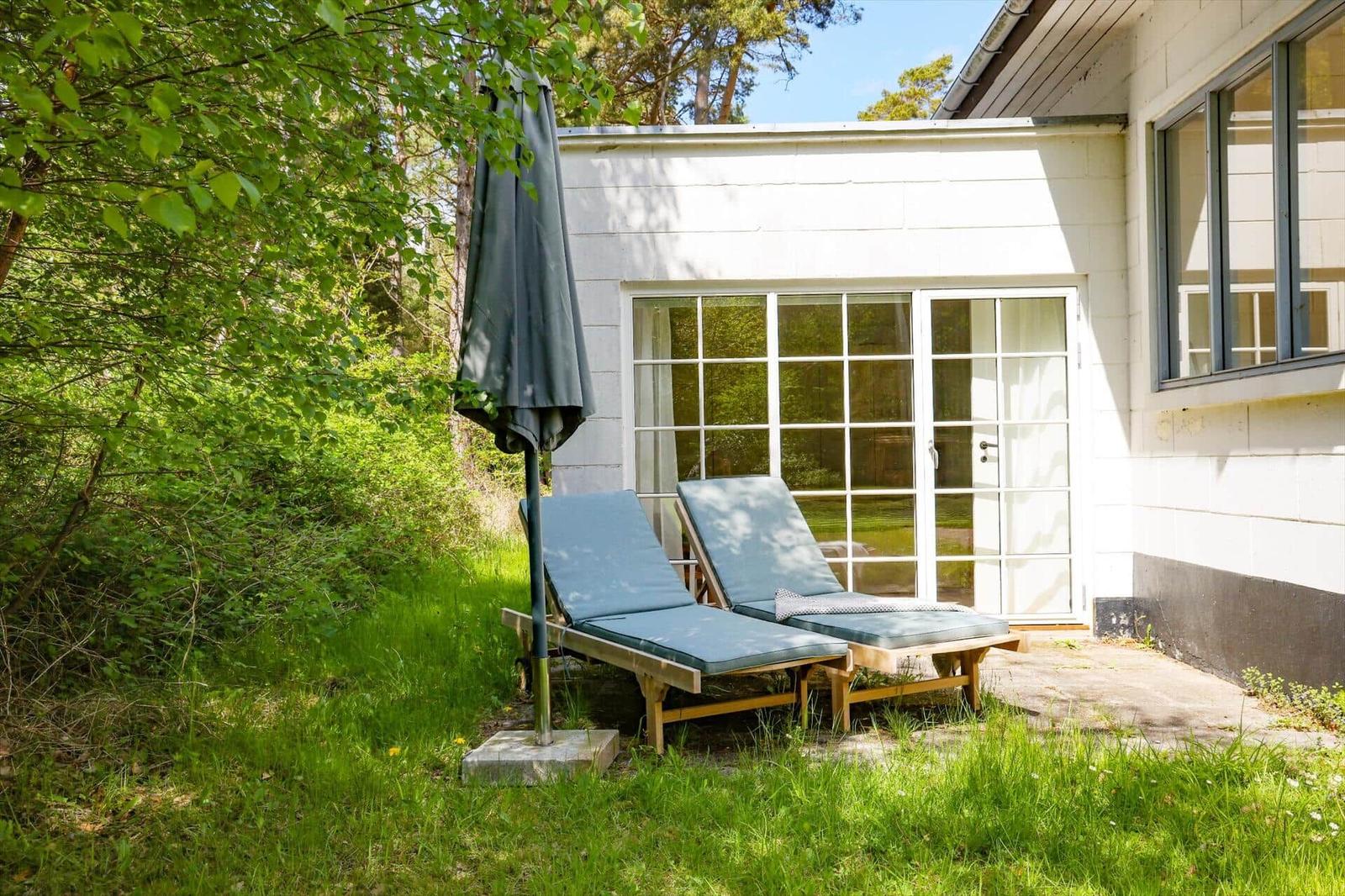 Zwei Liegestühle mit blauen Kissen stehen im Garten vor einem Haus mit Glastüren.