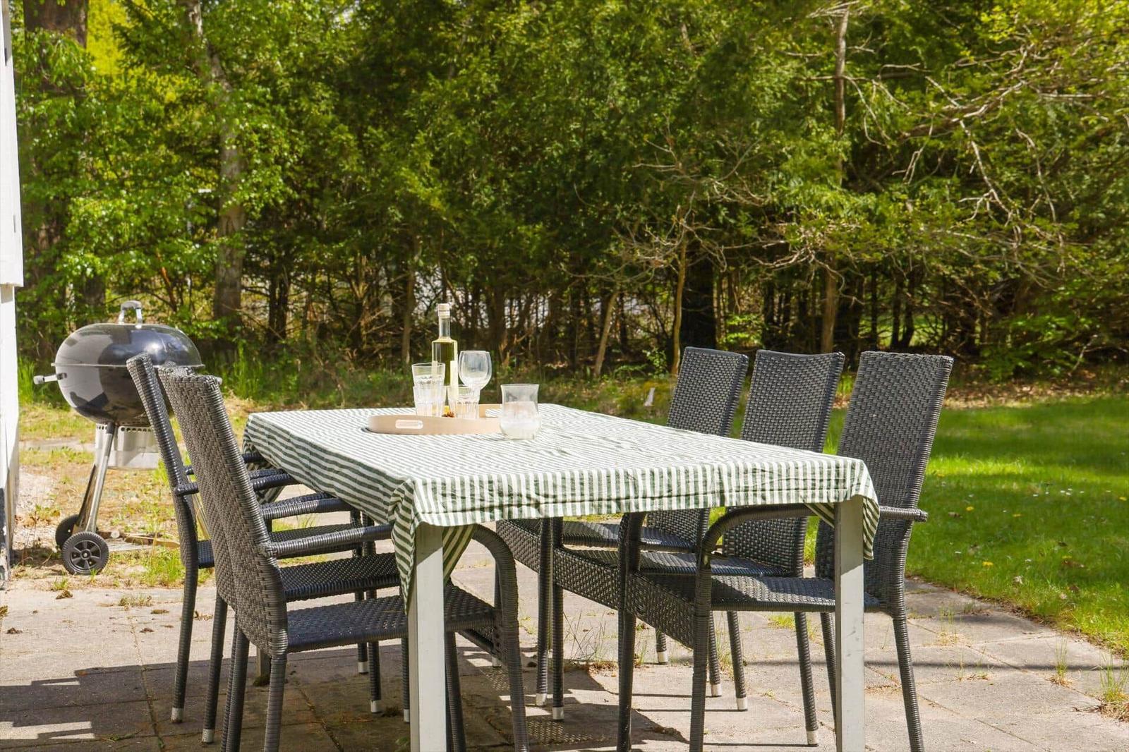 Außenbereich mit Tisch, Stühlen und Grill. Tisch mit Tischdecke und Gläsern.