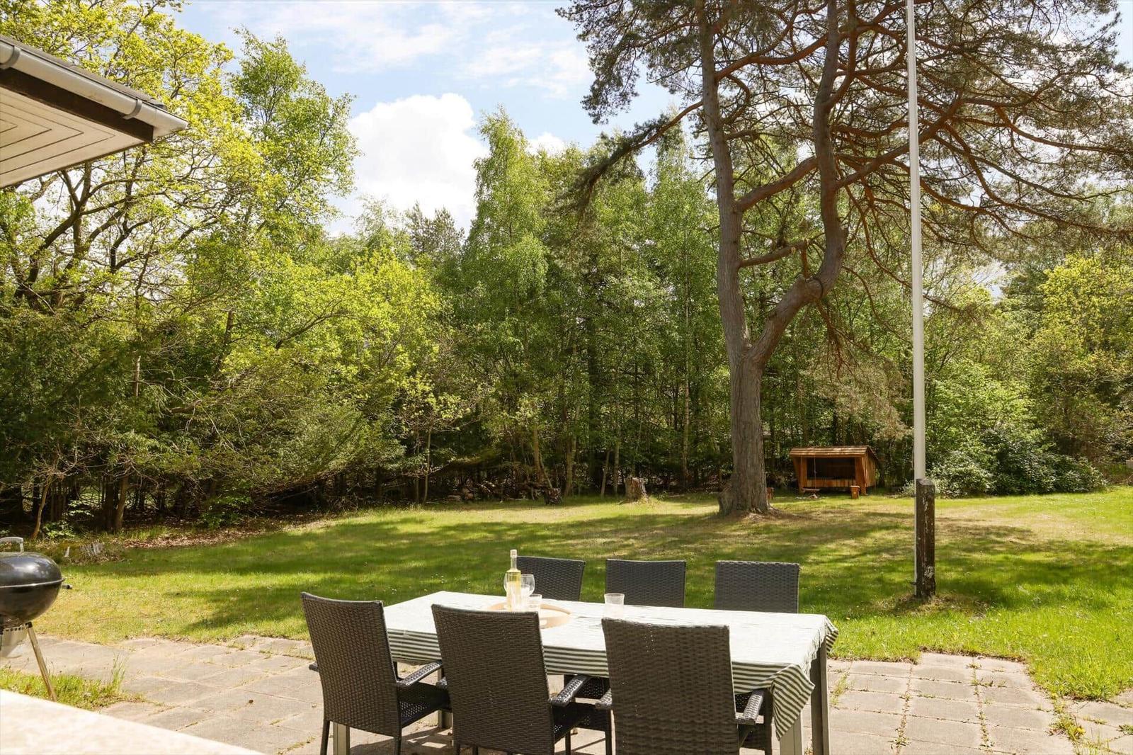 Garten mit Tisch, Stühlen und Grill unter Bäumen.