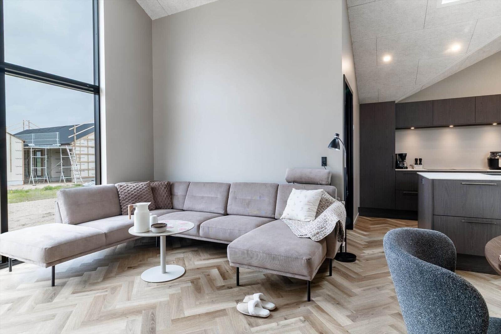 Wohnbereich mit grauem Sofa, Holzboden und Blick auf Baustelle.