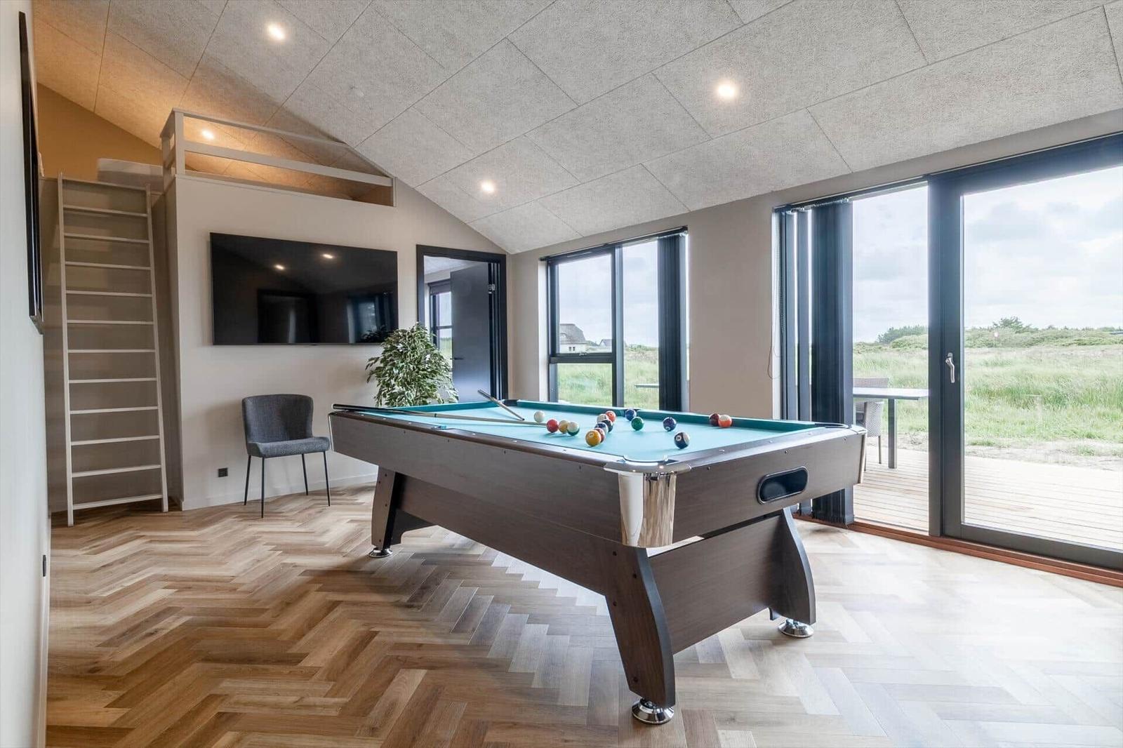 Raum mit Billardtisch, TV und Holzboden. Große Fenster mit Blick auf Grünland.