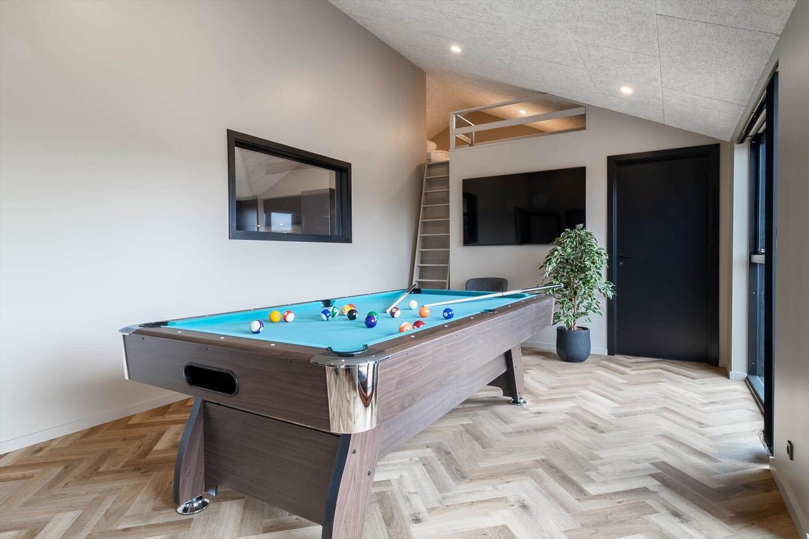 Billardtisch mit blauem Filz, Holzboden und Fernseher an der Wand.